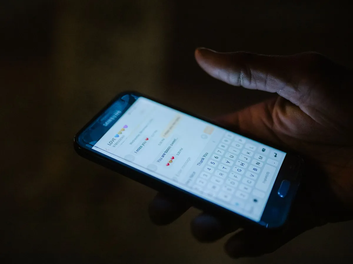 Gros plan d'une main tenant un smartphone avec une application de messagerie ouverte, éclairé par l'écran