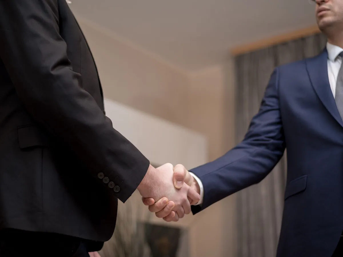 Deux hommes d'affaires en costume se serrant la main, en intérieur, pour sceller un partenariat