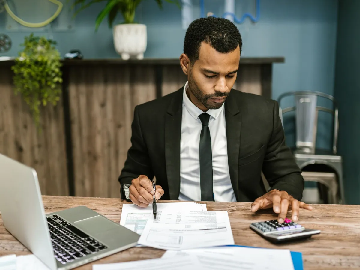 Homme d'affaires concentré, travaillant avec une calculatrice et des documents dans un bureau moderne