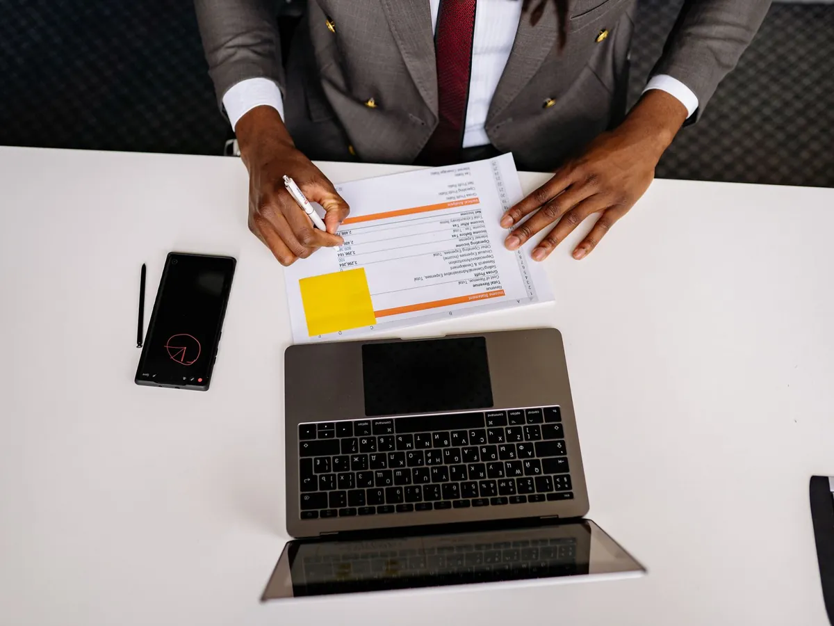 Vue de dessus d'un professionnel analysant des documents et son ordinateur portable sur un bureau blanc