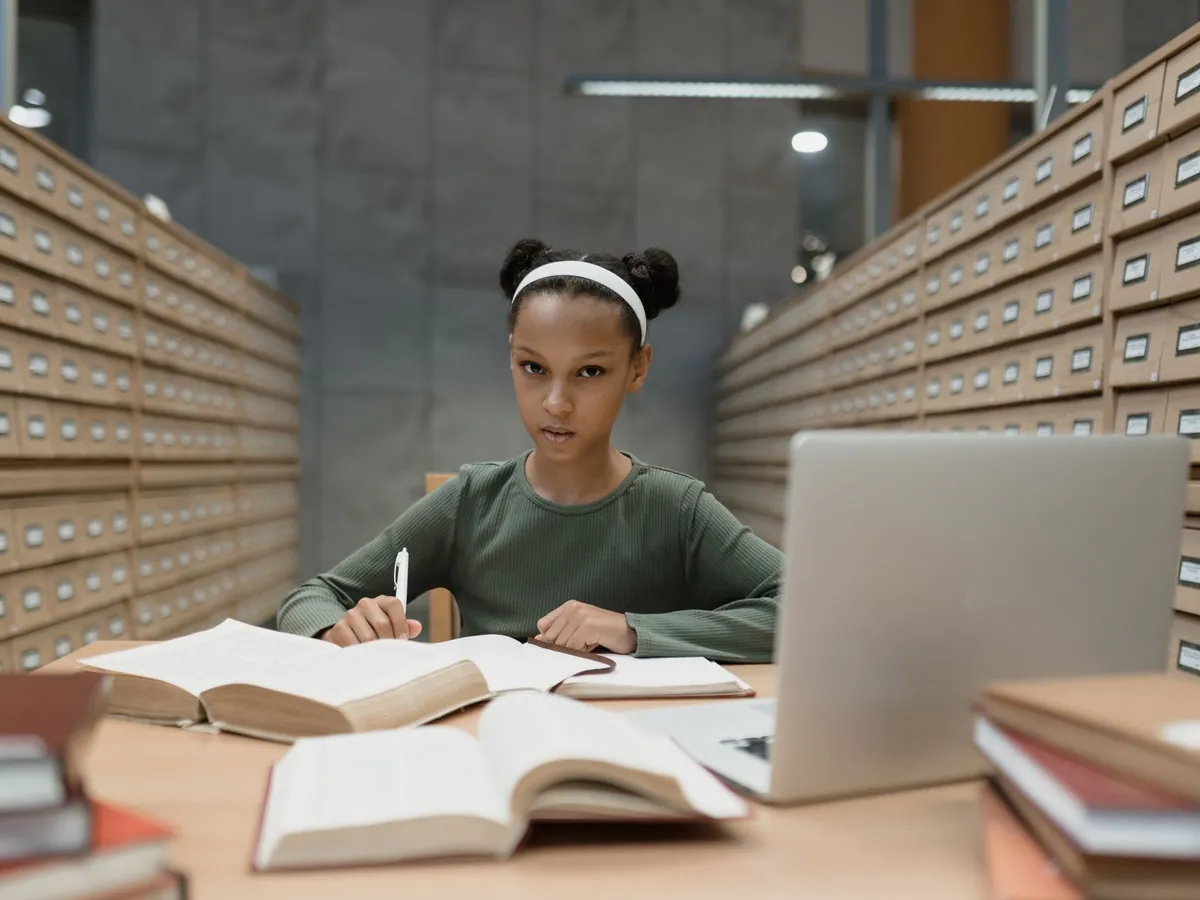 Jeune fille concentrée sur ses études à un bureau de bibliothèque, avec livres et ordinateur portable