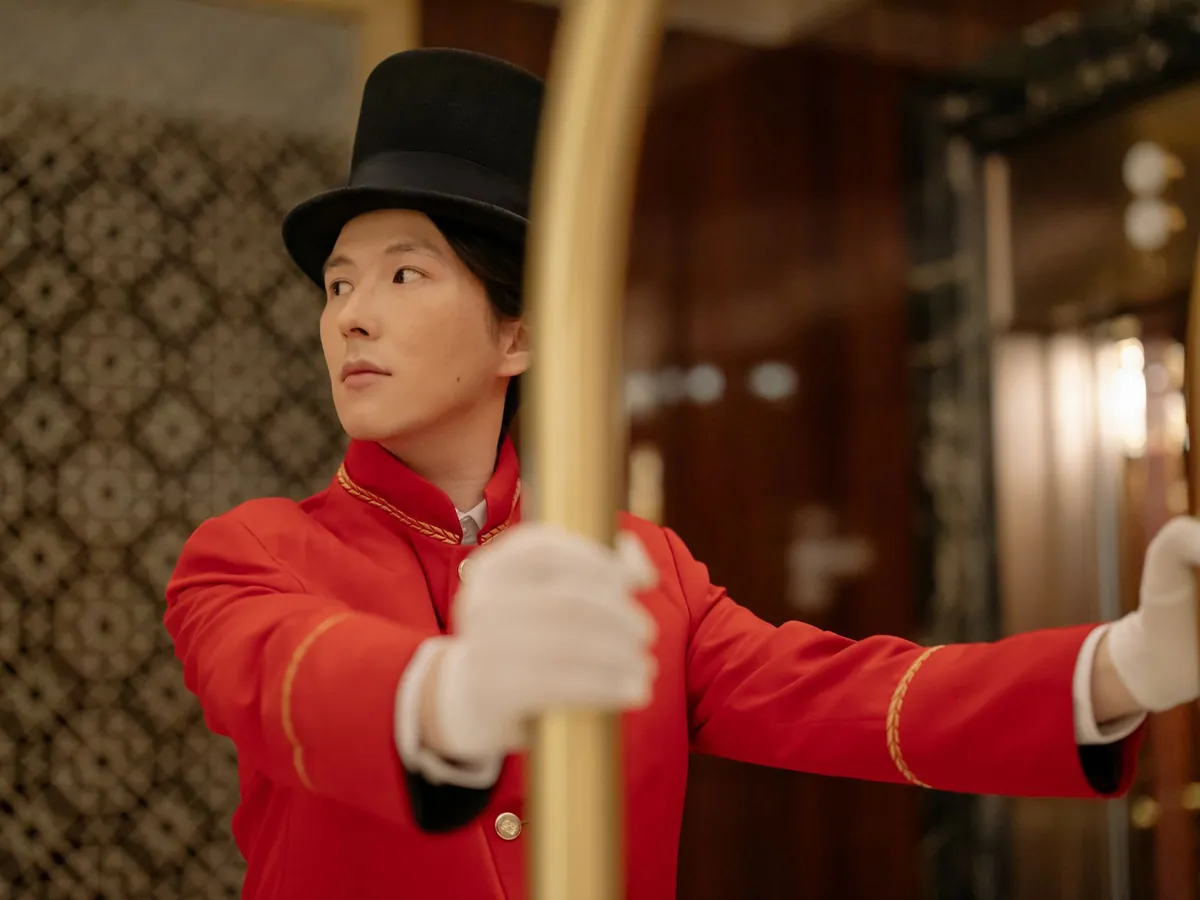 Chasseur attentif en uniforme rouge classique, poussant un chariot à bagages dans le hall d'hôtel