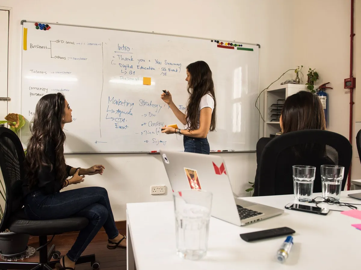 Femmes d'affaires discutant de stratégie devant un tableau blanc dans un bureau moderne