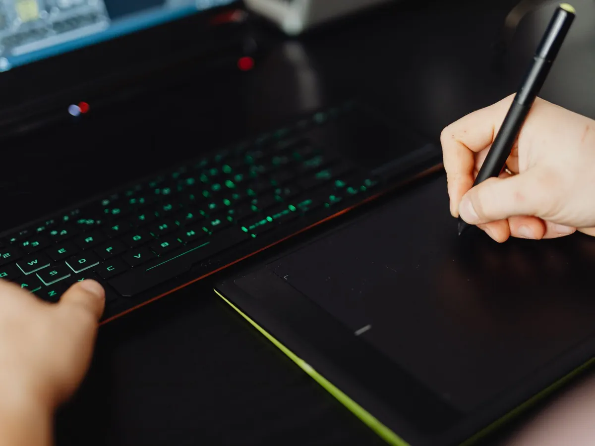 Gros plan de mains dessinant sur une tablette numérique avec stylet, création artistique sur un bureau