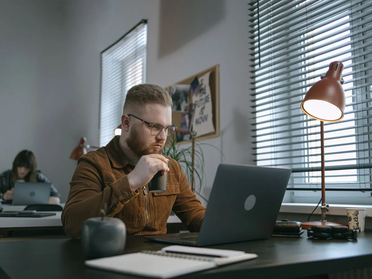 Homme barbu buvant un café en travaillant sur son ordinateur portable dans un espace moderne