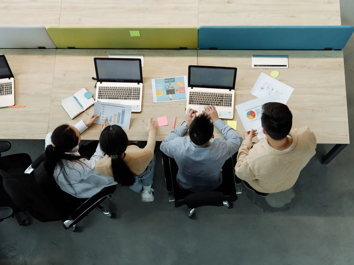 Vue aérienne de quatre collègues travaillant sur ordinateurs portables et documents, autour d'un bureau partagé
