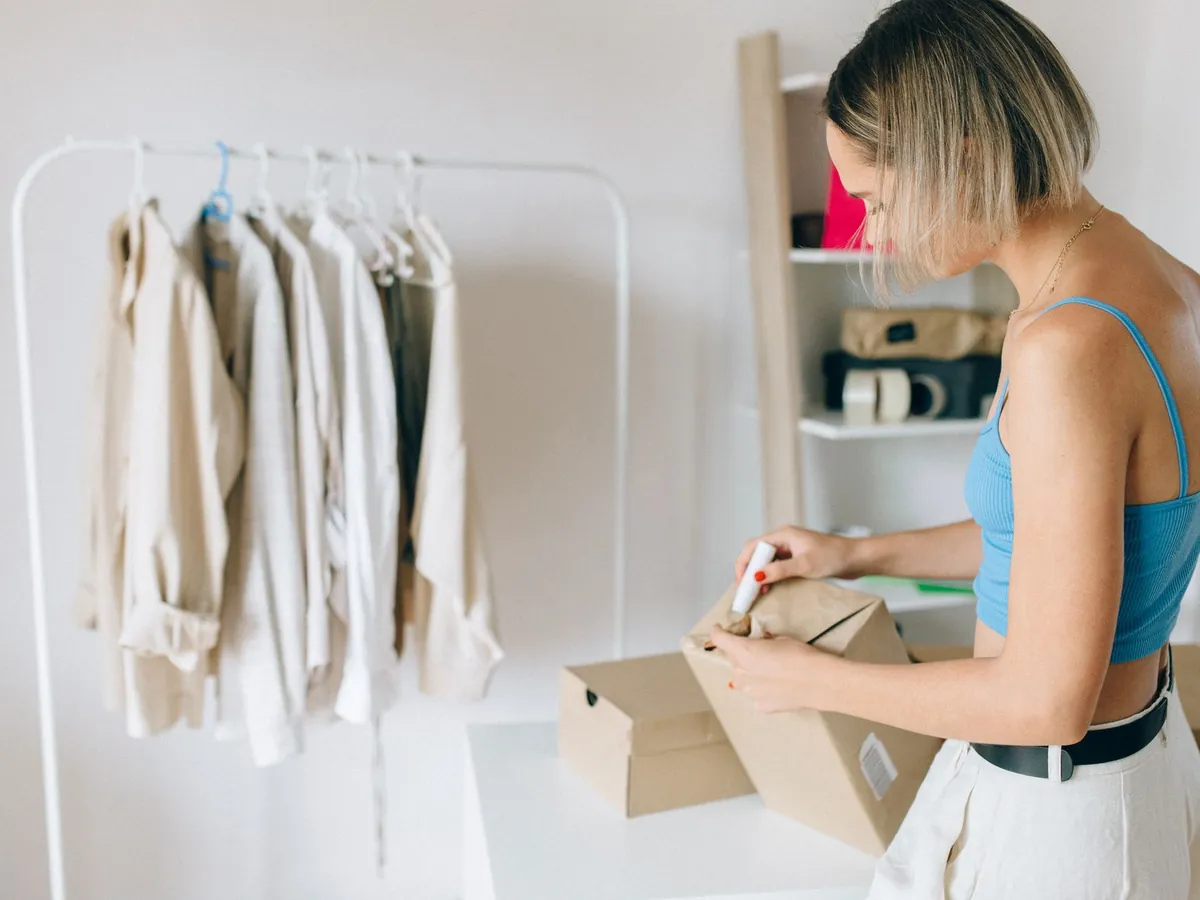 Commerçante en ligne préparant un colis près d'un portant de vêtements
