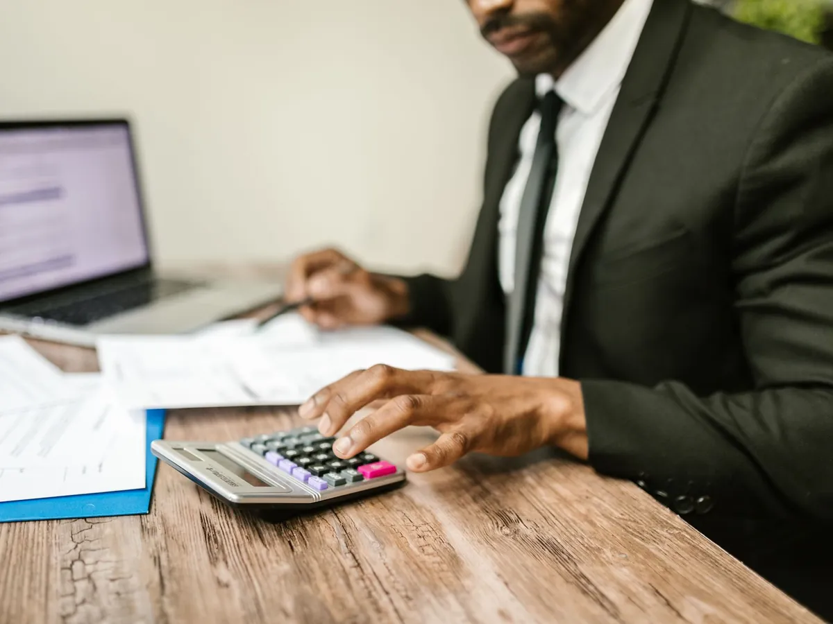 Expert-comptable en costume utilisant une calculatrice devant son ordinateur