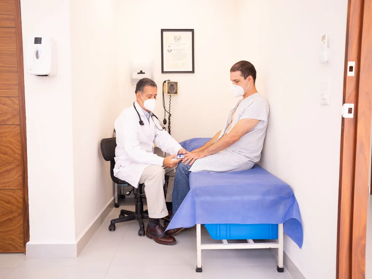 Médecin masqué examinant un patient assis sur une table de consultation