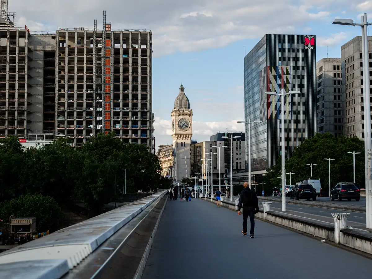 Vue d'un pont urbain avec des piétons et une tour horloge au loin, entourée de grands immeubles