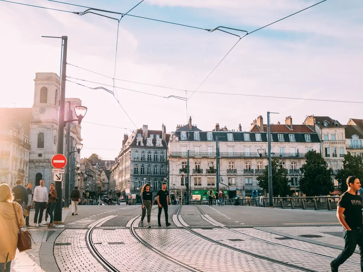 Passants traversant un carrefour de tramway ensoleillé dans une ville historique européenne