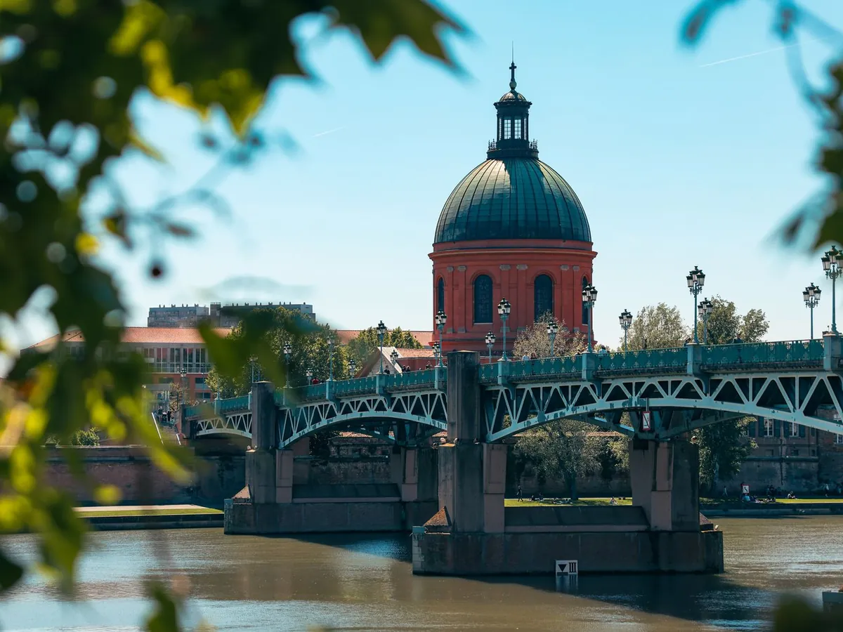Vue sur le pont Saint-Pierre et le dôme rouge de Toulouse, encadrée de feuillage