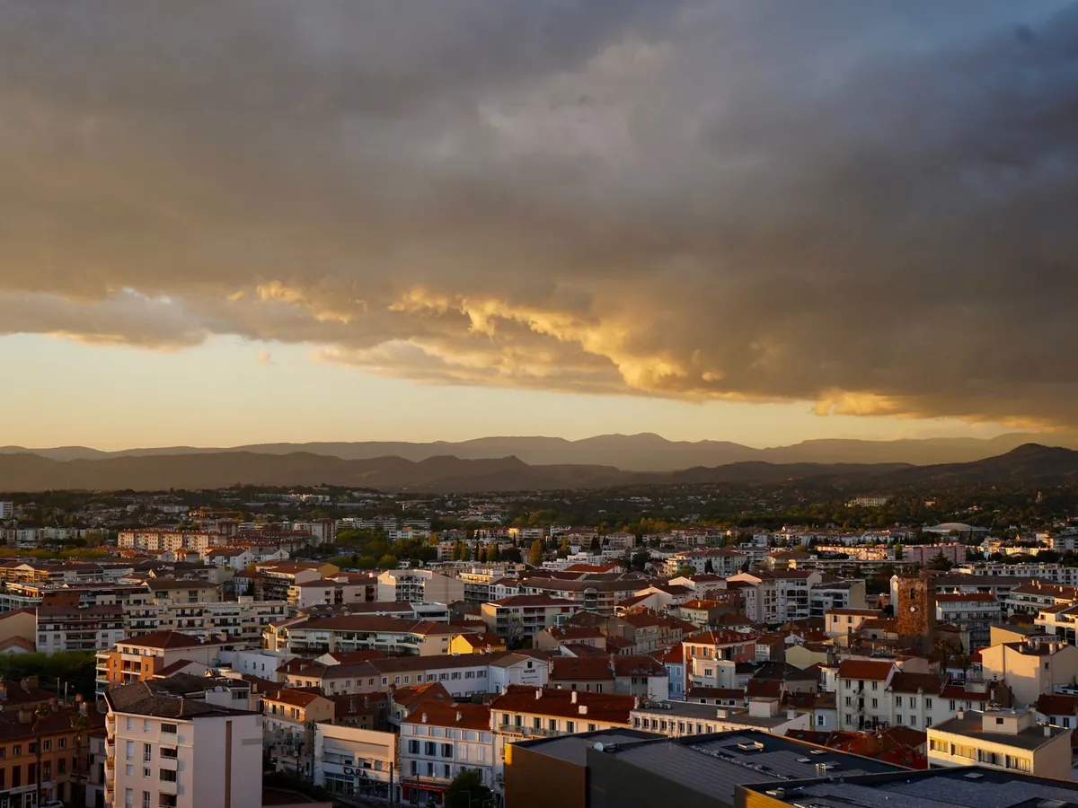 Paysage urbain spectaculaire sous un coucher de soleil dramatique, avec des nuages et des montagnes au loin